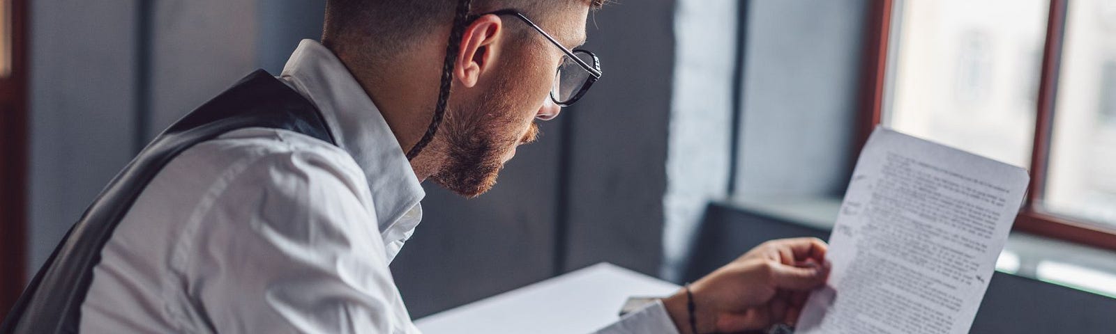 Young bespectacled man in business shirt and vest studies full page on an ancient typewriter.