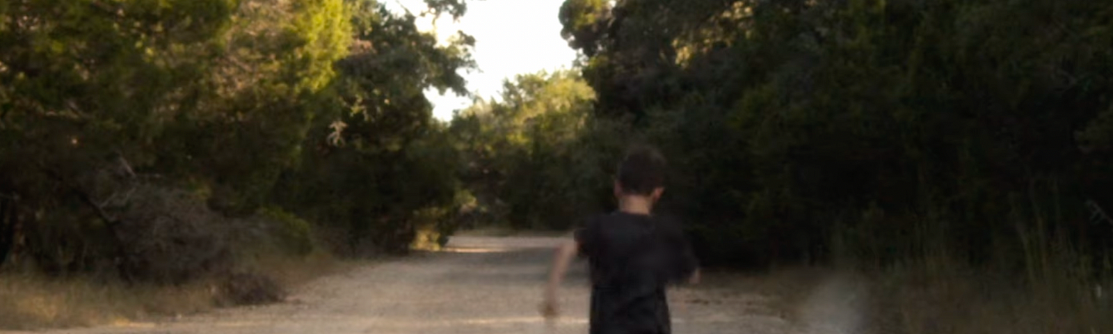 Photo of a young boy running down a road in the woods.