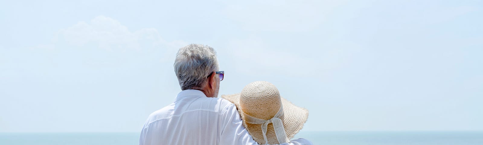 Mature couple standing together with arms around each other enjoying the ocean view.