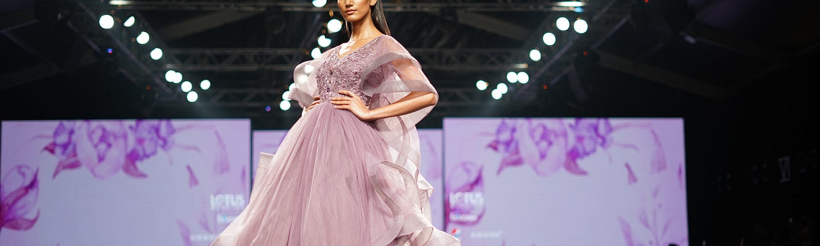 A runway model strikes a confident pose in a lovely dress for spring in a fashion show.