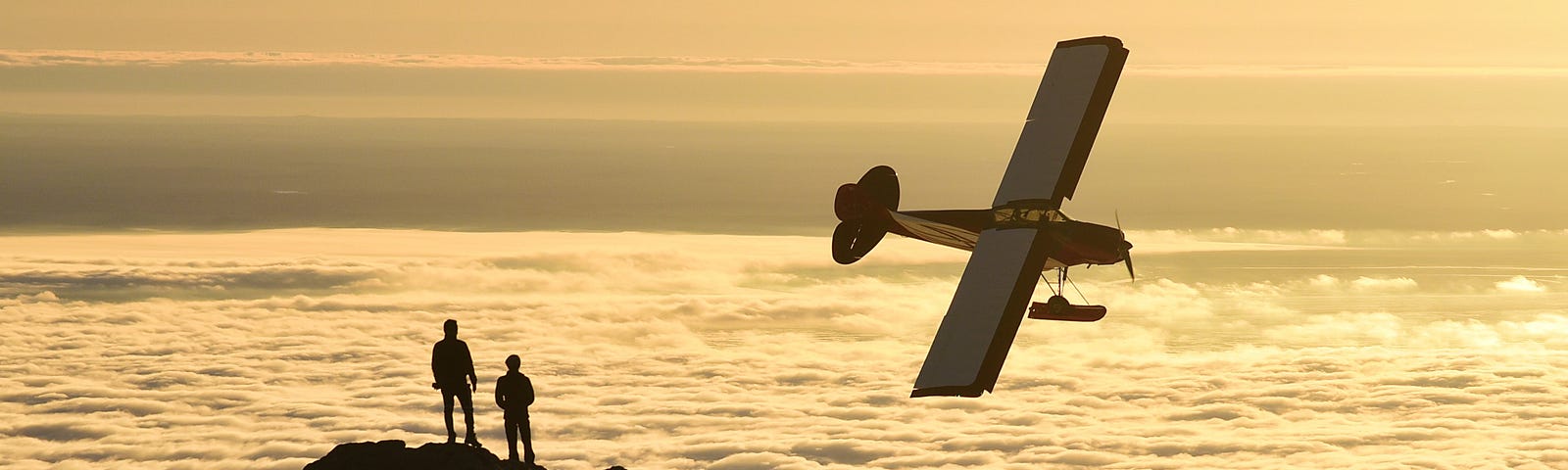 Two people stand on a mountaintop as a single-engine prop plane banks above a sea of clouds…Broken Rainbows by Jim Latham | Photo by Paxson Woelber on Unsplash