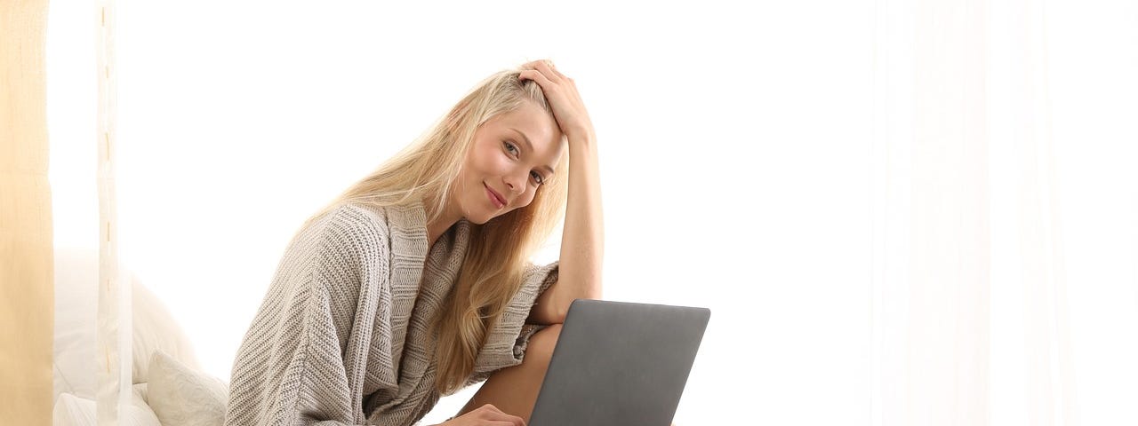 Woman sitting on her bedm, look at her computer.