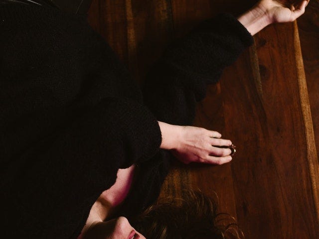 Photo Description: A woman dressed in black is laying on the floor with a look of life is absolutely over. She has reached her limits. Her wedding ring is off her finger laying on the floor next to her.