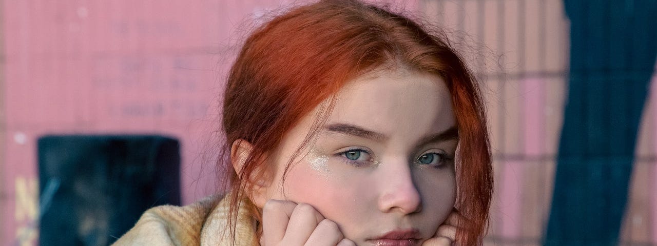 A teen with red hair holds her face in her hands, deep in thought