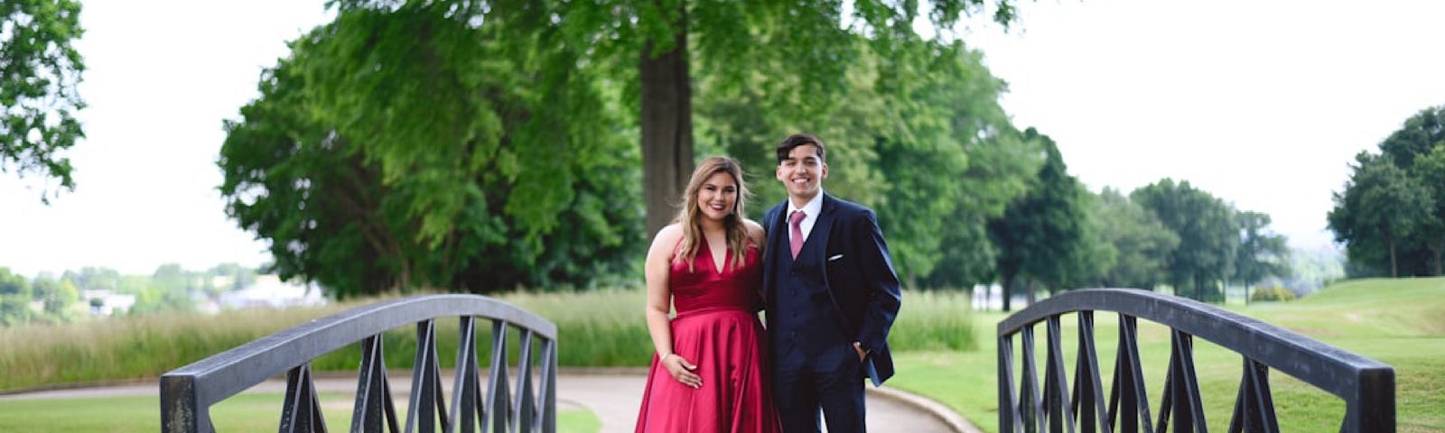 A young woman and a young man dressed for prom posing for a photo on a bridge.