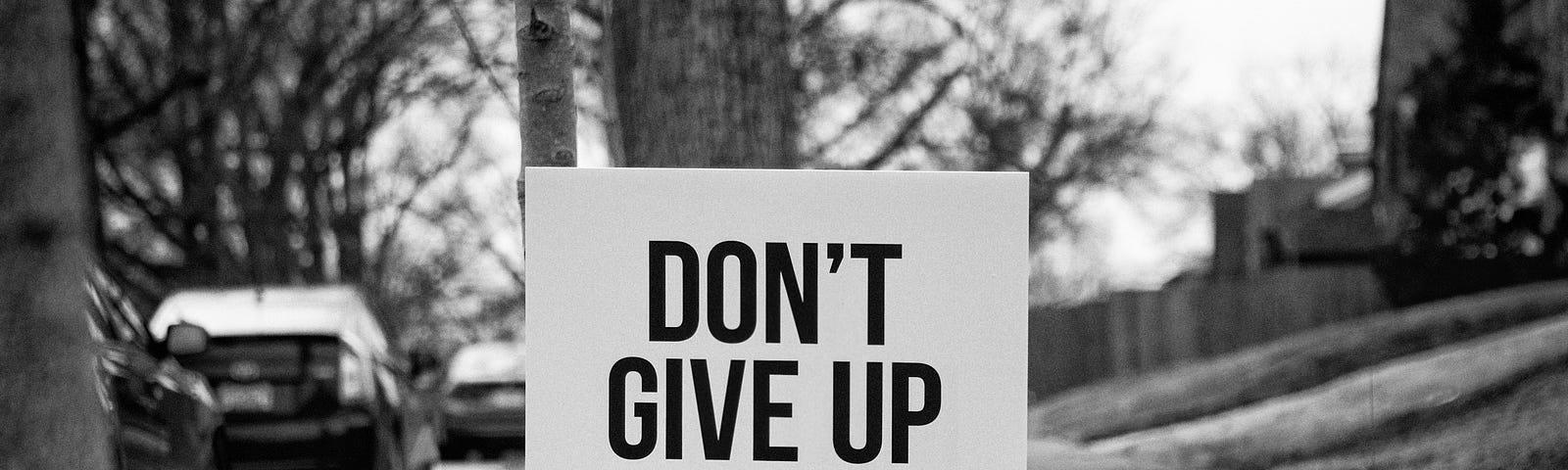 sign next to a sidewalk reading “don’t give up”