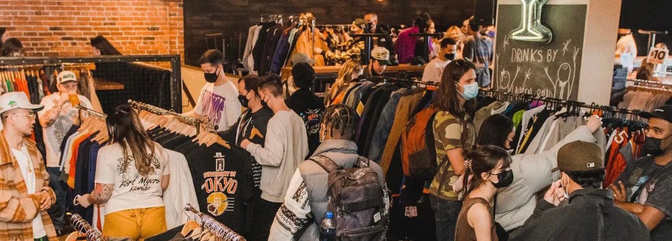 Shoppers look through racks of clothing in an industrial-style building.