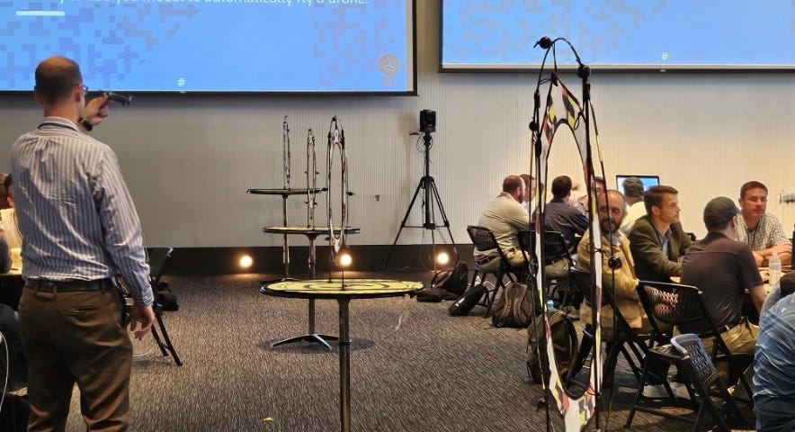 A group of people in a room with a projector are calibrating their drones to navigate targets.