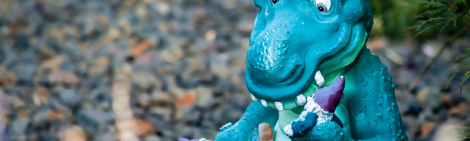 A blue plastic dinosaur looking down at two gnomes he holds in his hands.