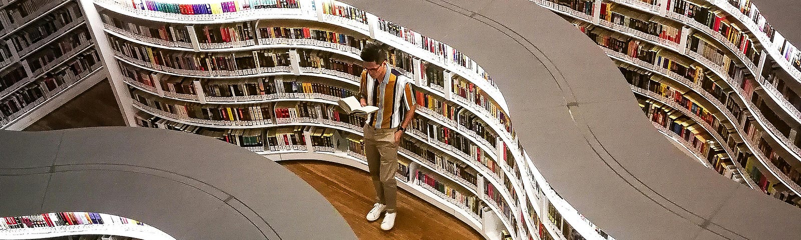 Man reading a book amidst the curving shelves of a library or book shop.