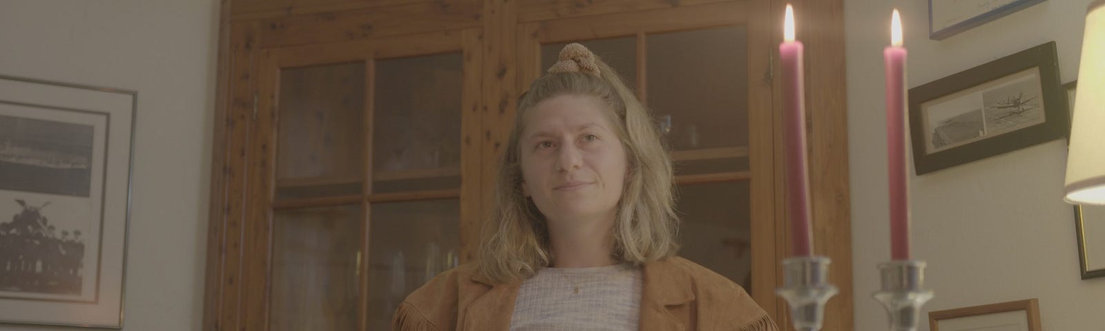 A headshot of Shoshana Ehrenkranz in front of a wooden cabinet and behind two lit candles.