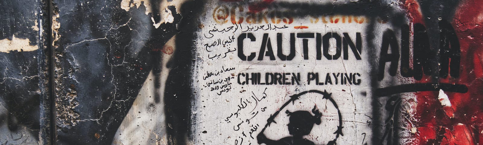 graffitti on a wall that says “caution children playing with barbed wire”