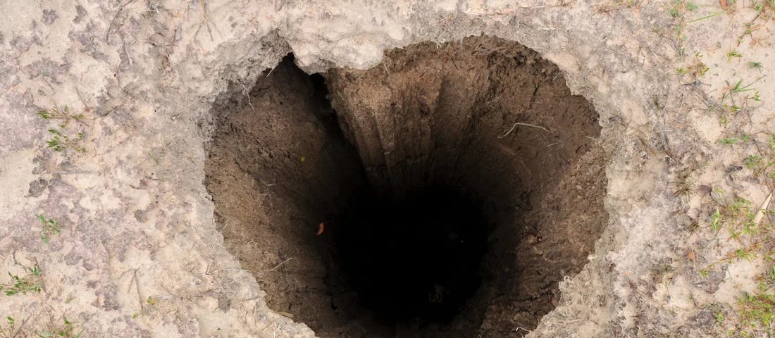 Deep hole in the ground with a vague heart shape to its entrance.