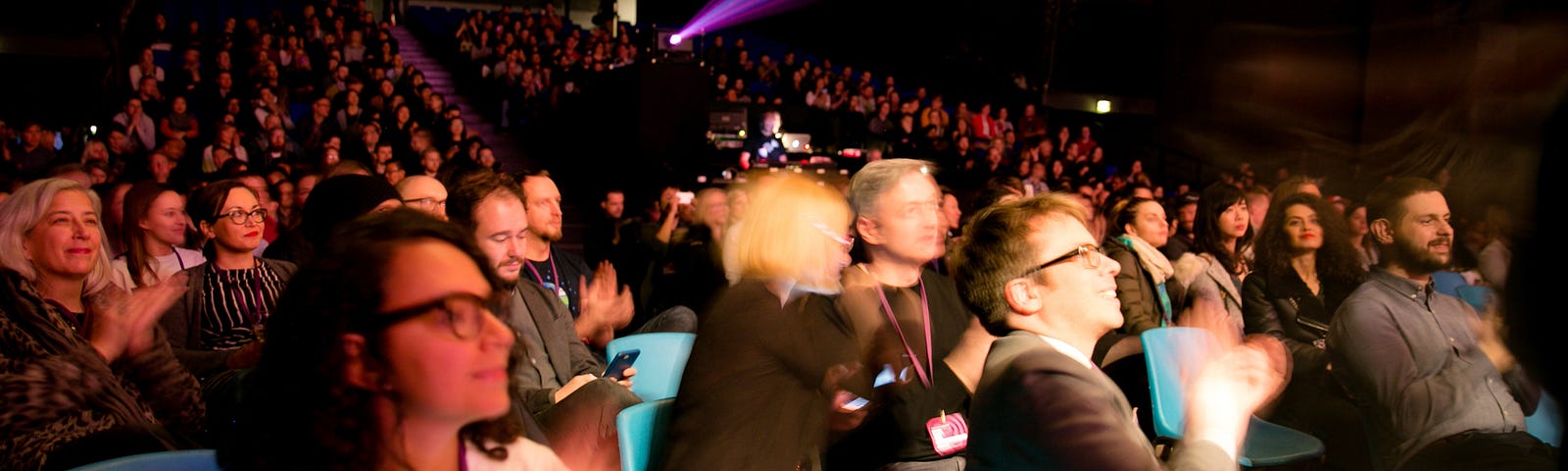 An audience of Interaction Awards attendees applaud. They are seated in a theatre and looking at the stage which is out of frame to the right.