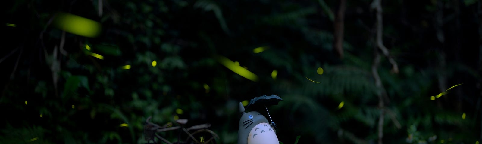 Small figurine of Totoro with umbrella on mossy log in dark forest.