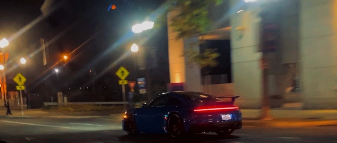 a midnight blue sports car (Porsche maybe) speeding down the empty city streets, after midnight.