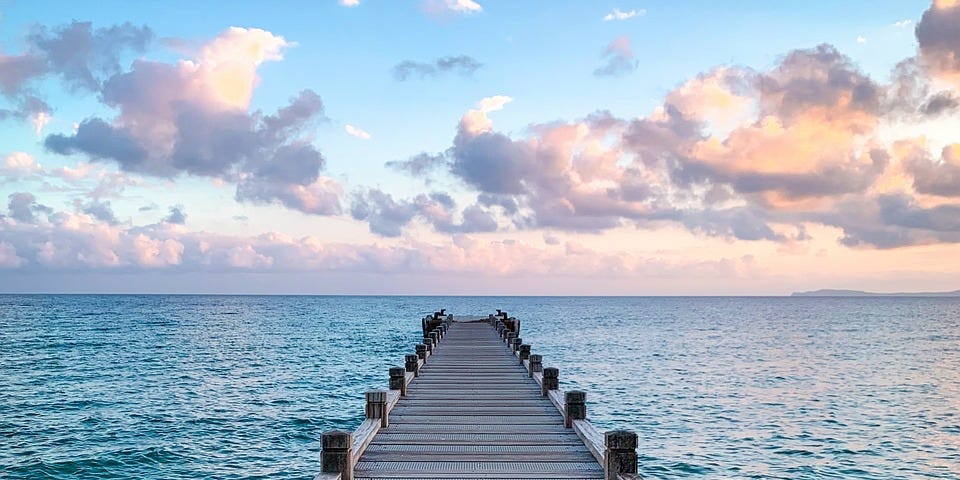 A woman sitting alone on a jetty watching the ocean.