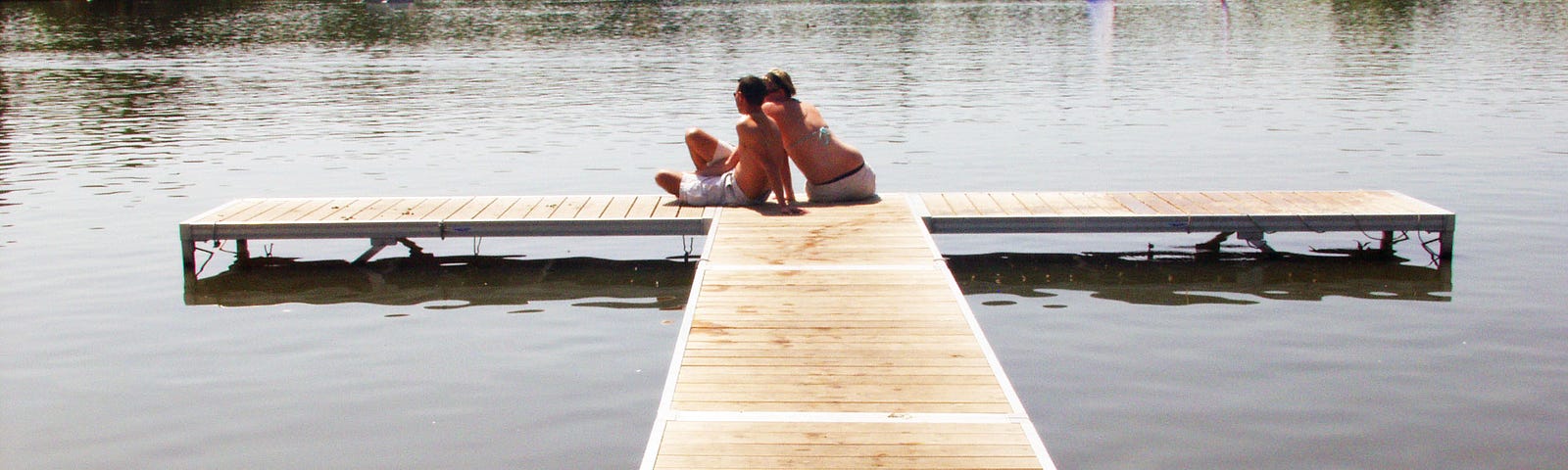 Couple sitting on a pier at the edge of a lake.