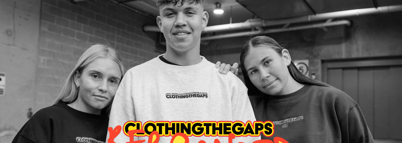 A black and white photograph of three people, with the two people on the outside leaning on the taller person in the centre. They all wear jumpers that say ‘Clothing the Gaps’ in small writing across the chest. On the bottom of the image is a logo for Clothing the Gaps in red, yellow, and black, with red handwriting and yellow highlights underneath reading ‘Rebranded’.