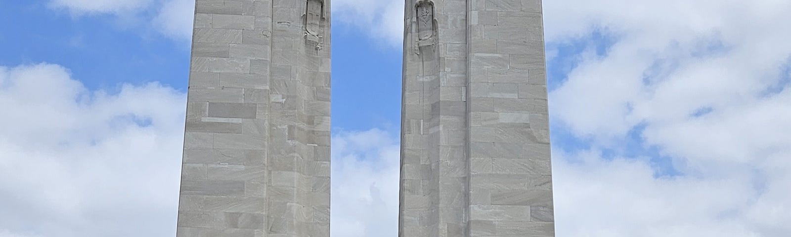 Two pillars rise 27 meters from the base of the Vimy Ridge Memorial, with sculptures carved into the pillars.