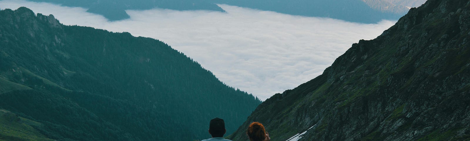 Photo of a man and woman together on a dark, high vista, looking at a lighted valley in the mountains with a lake.