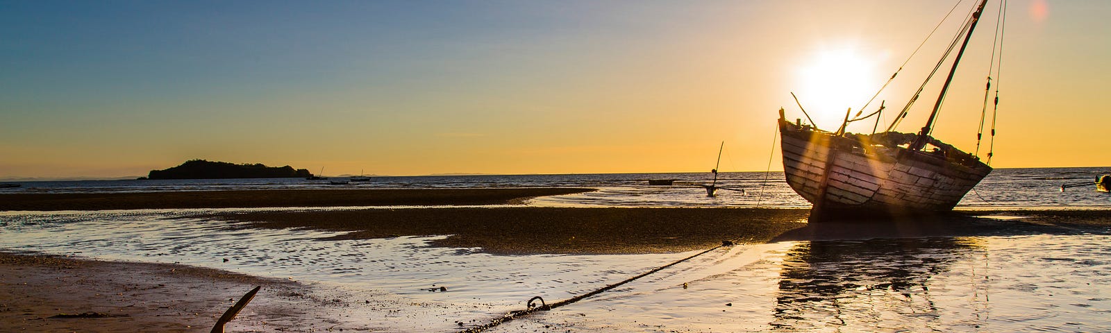 Boat on a beach with anchor securing it with a setting sun.