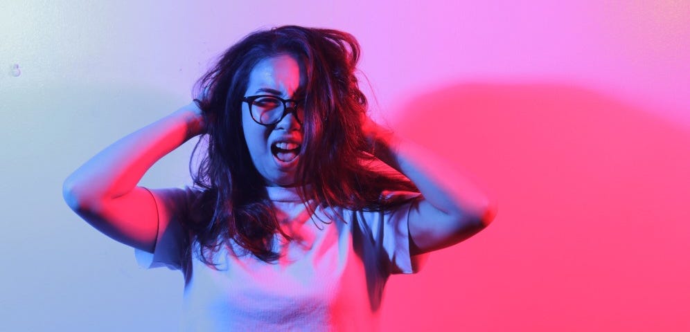 A woman screams and ruffles her hair against a blue and pink background. People who are bad for your self-esteem.