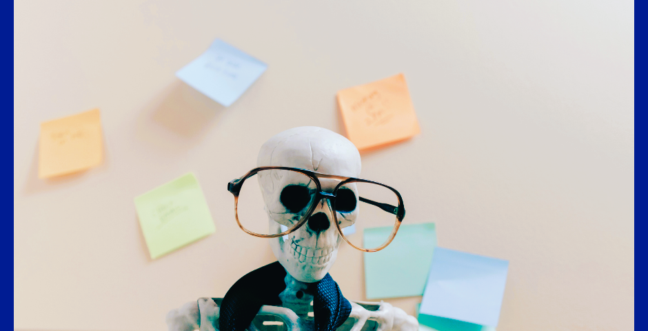 skeleton at a desk wearing eyeglasses and papers strewn about