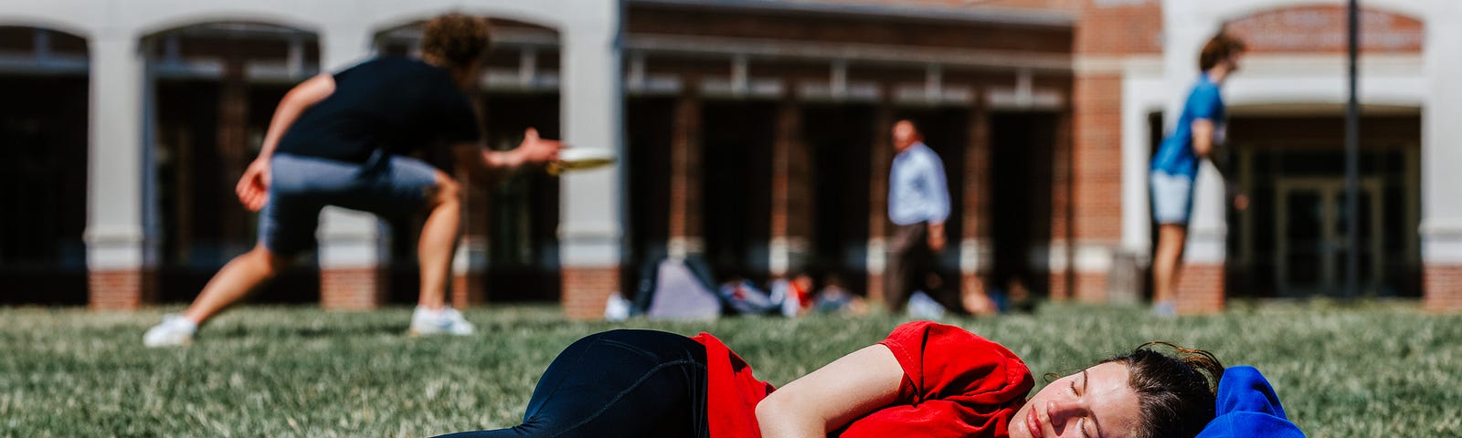 A student relaxes in the sun on the greenspace