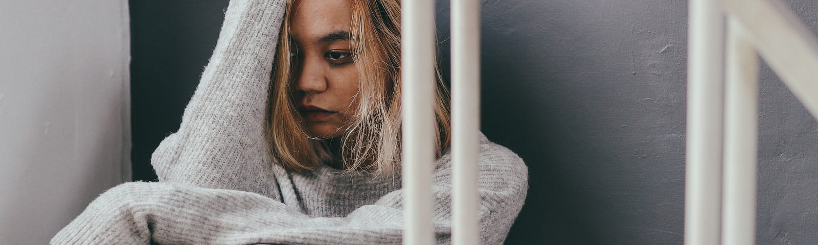 A dishevelled young woman sits in a stair with her knees folded up and an arm resting against her head.