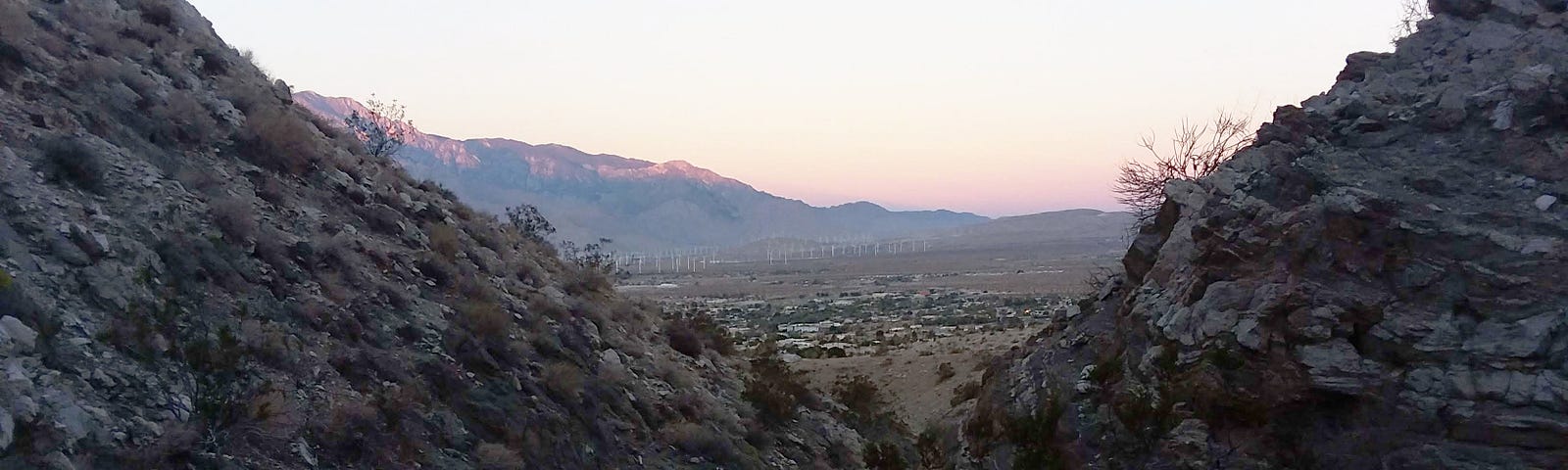 Two rocky nearby hills parting to reveal a valley with a town, windmills, and mountains on the horizon.