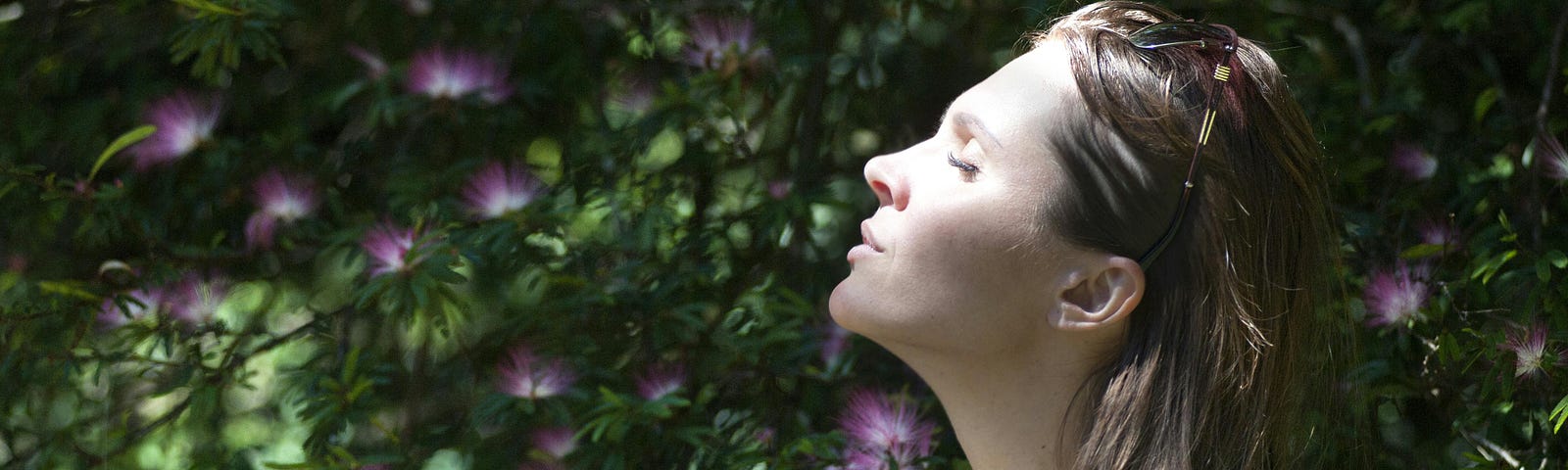 A woman breathing consciously in front of a flowering bush