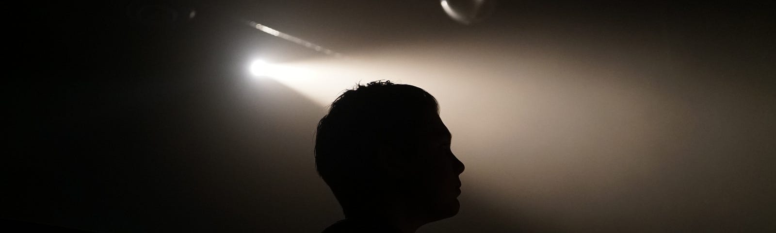 Side view silhouette of a head in a dark place with a ray of light from an opening above to the side.