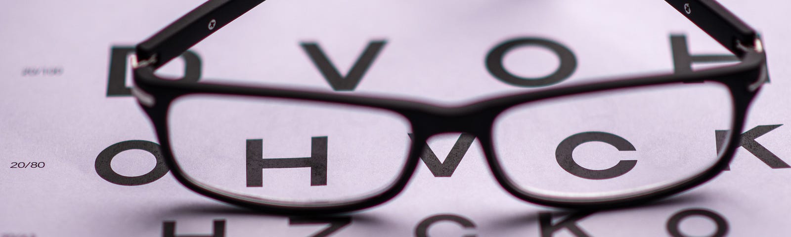 A pair of black eyeglasses sits on top of an optometrist’s eye chart.