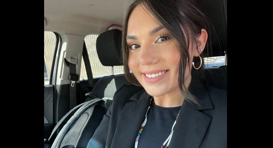 Lorell Ward sits in a car and smiles at the camera, wearing a beaded necklace and black blazer