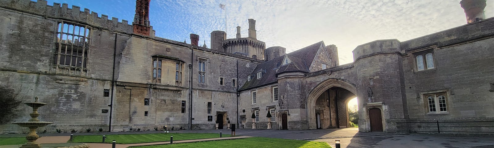 The exterior of Thornbury Castle near Bristol, England, featuring the fountain courtyard, late afternoon sun and a blue sky. Photo by Laura Metze.