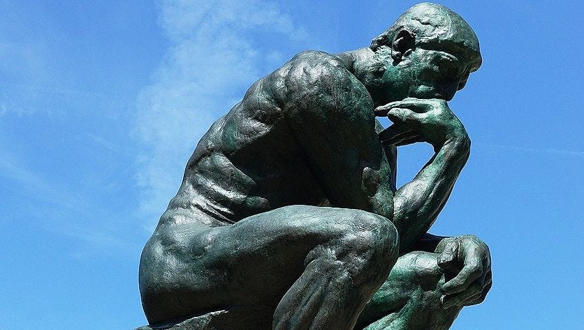 Statue in bronze with a background of clear blue skies: a man is sitting with his hands on his knees, thinking.