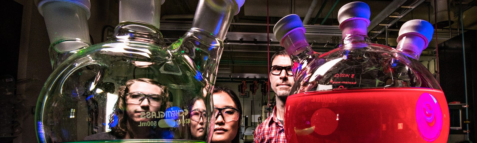 Four people sitting behind two glass tubes with colorful liquids