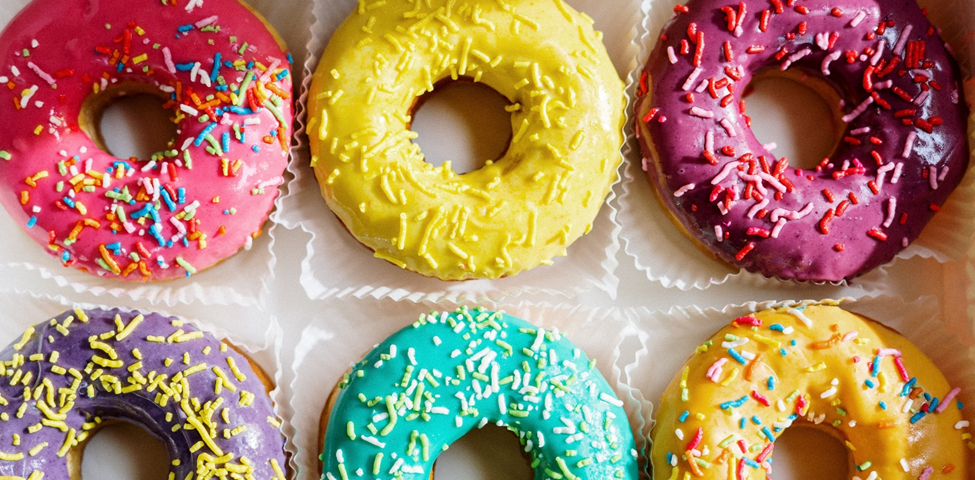 Six donuts with sprinkles, each with a different color of icing