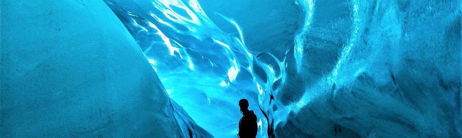 silhouette of man in blue ice cave