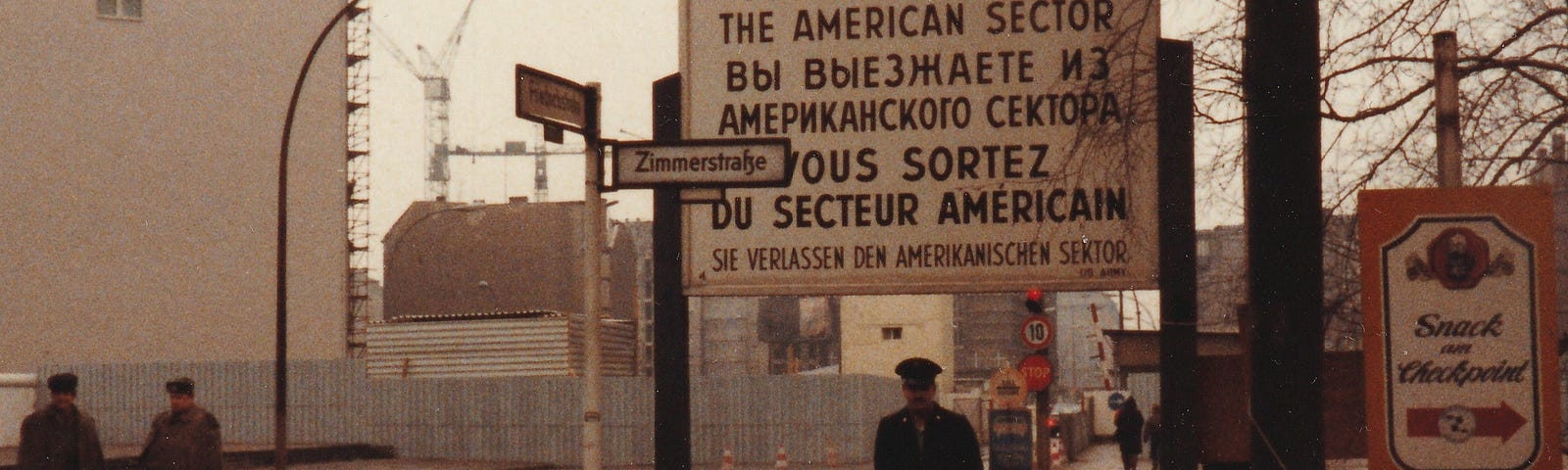 The author, standing on the western side of Checkpoint Charlie, Berlin. November, 1984. The sign above him, in four languages, reads: “You are leaving the American Sector.”