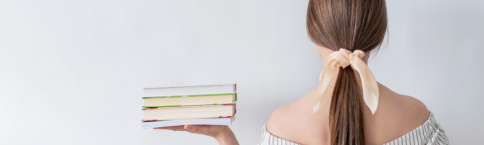 A girl stands with her back to us, holding a stack of untitled books