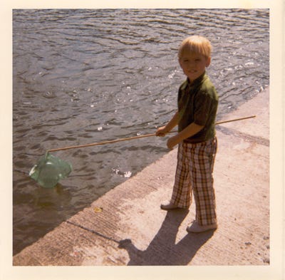 Photo of author in plaid pants as a little boy. I’m holding a fishing net and standing next to a body of water