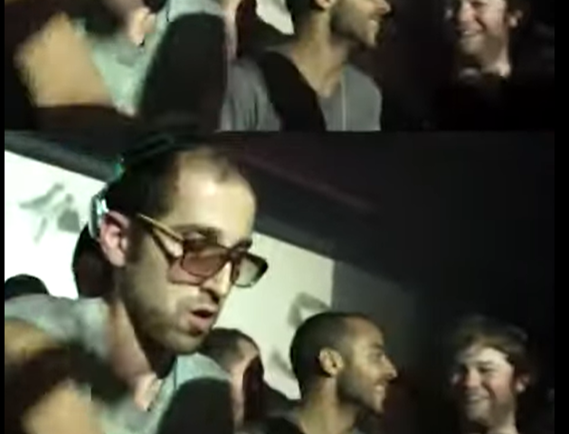 An image of a rave it is dark with many people around in a club with lights flashing and Thomas Bangalter a thin man with glasses wears headphones as he DJ’s for the club goers around.
