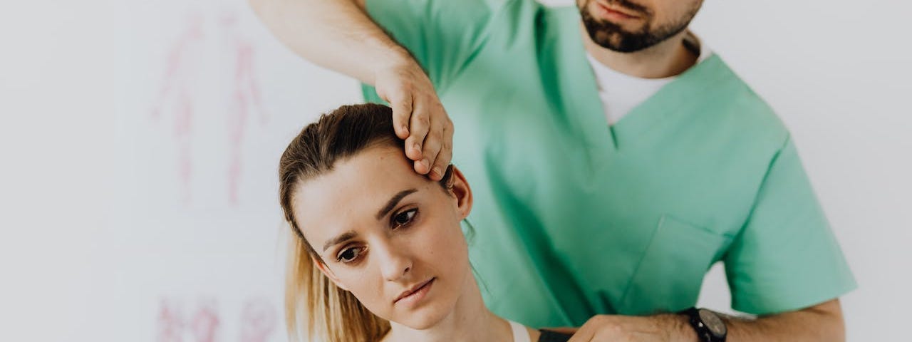 A physical therapist presses gently on a dark-haired woman’s head, stretching her neck in the process