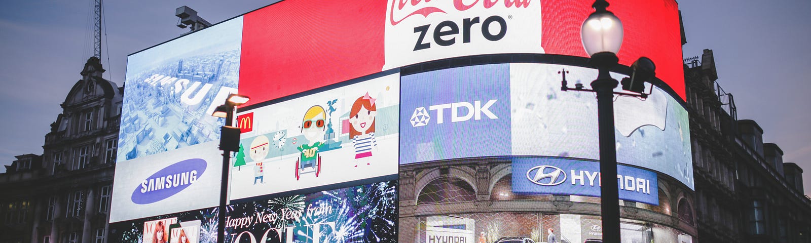 A foto apresenta uma esquina com diversas placas com marcas como Coca-Cola, TDK entre outras