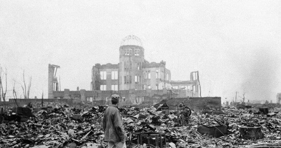 An man stands in front of the shell of a building after nuclear attack in Hiroshima by America on Aug. 6, 1945.