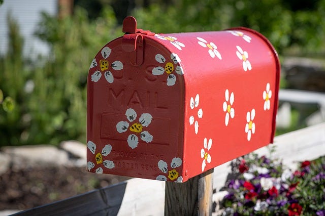 Red painted mailbox, decorated with a flower pattern, painted daisies, fence and trees in the background