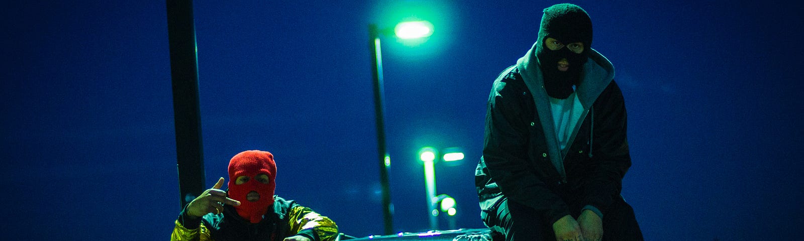 two masked men sit outside a car