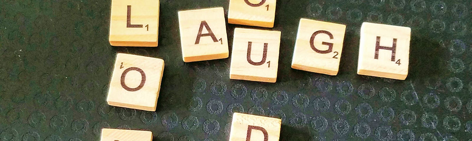 Messy crossword made of wooden letter tiles spelling out: Laugh, long, loud